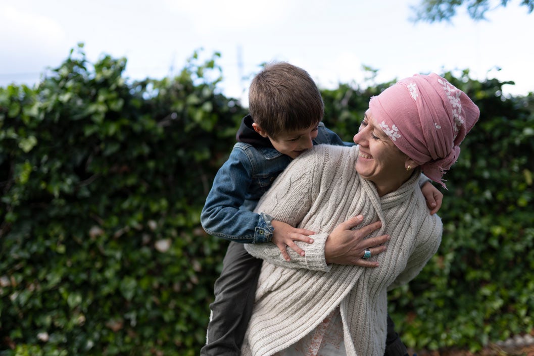 Mother with cancer and wrap on her head hugs son in backyard