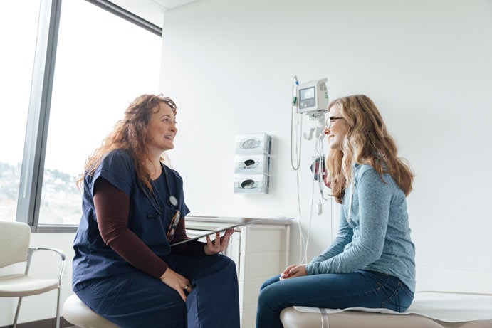 Woman in exam room speaking with a doctor in scrubs